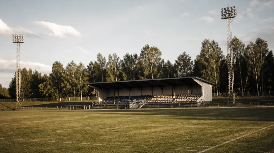 Fotbollsplan sedd från läktaren i grått dagsljus med tomma sittplatser i förgrunden