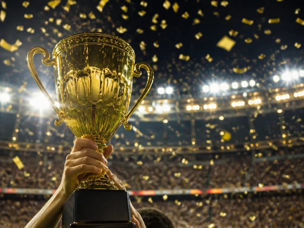 Gyllene pokal lyfts i ett upplyst fotbollsstadion med guldkonfetti i luften